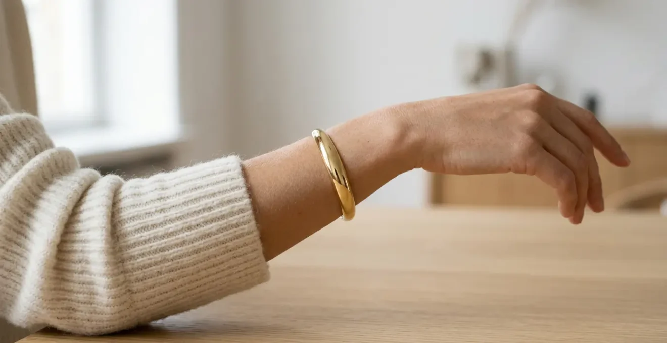 Gold cuff bracelet elegantly positioned over cream wool knit sweater sleeve