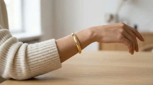 Gold cuff bracelet elegantly positioned over cream wool knit sweater sleeve