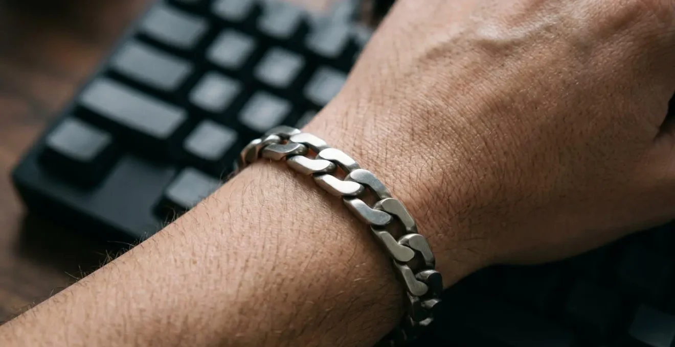 Man's wrist with thin silver bracelet positioned at keyboard typing angle